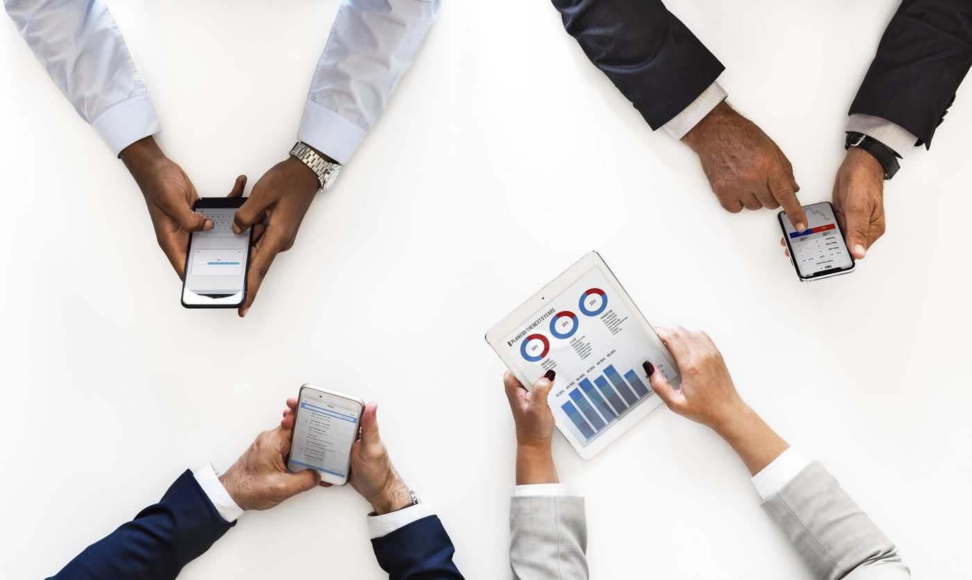 Hands holding phones and a tablet showing financial charts